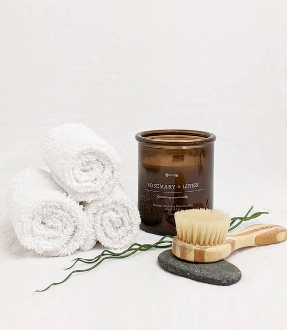 BrowBone spa wellness arrangement with rolled towels, scented candle and wooden body brush