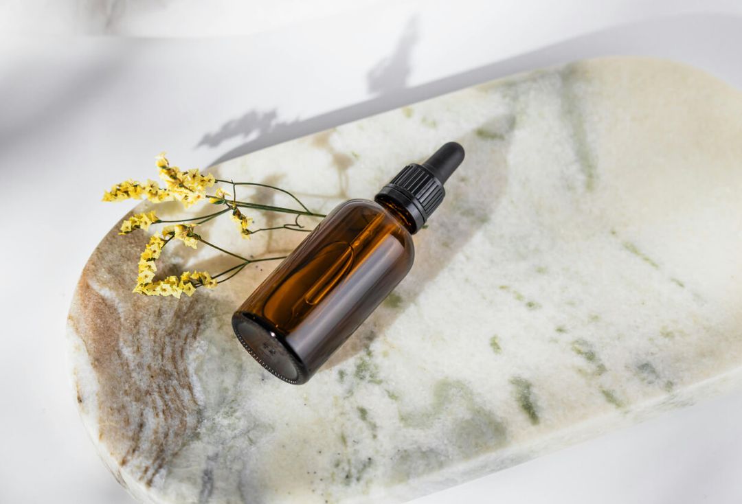 Natural skincare oil bottle on a marble stone with yellow flowers